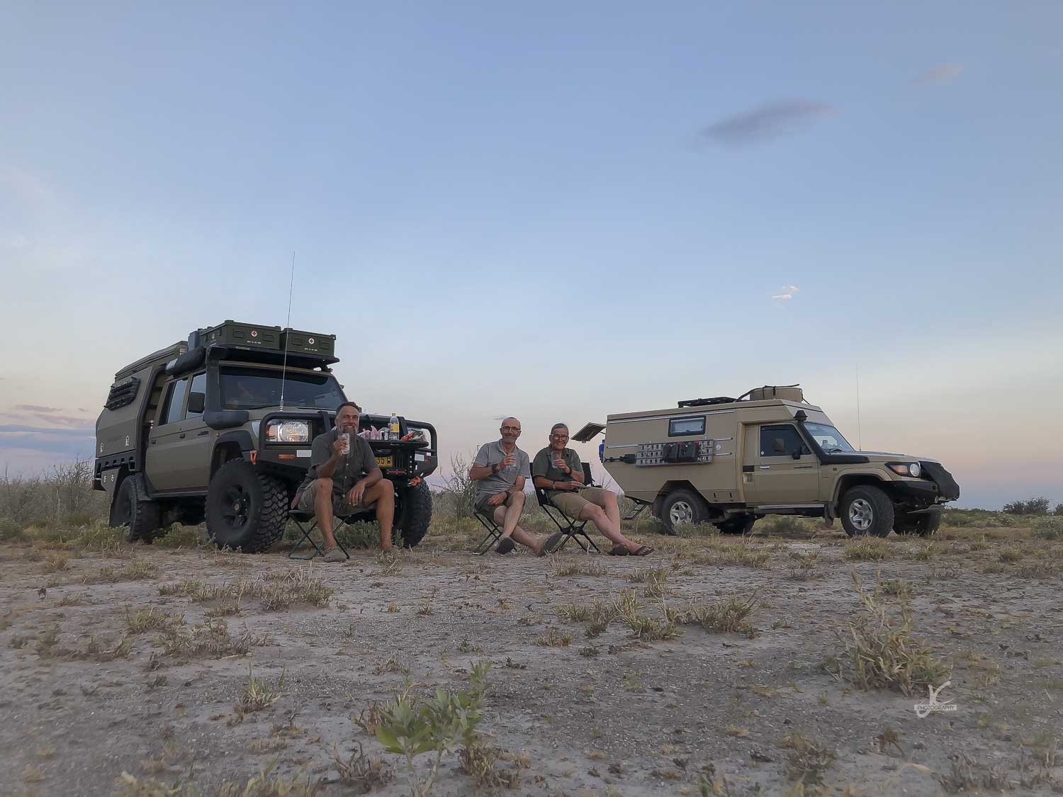 Three travelers seated beside two expedition vehicles
